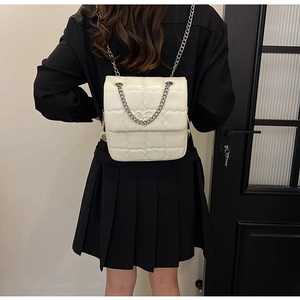 Close-up of a white quilted chain crossbody bag featuring a golden heart logo on a model