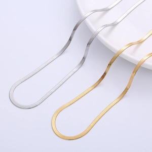 Flat 3mm stainless steel snake chain necklace in gold and silver finish on a white plate