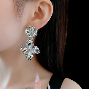 Close-up of oversized silver floral earrings featuring double layer metallic flower design