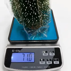 Detailansicht eines beschneiten Mini-Weihnachtsbaums beim Wiegen auf einer Digitalwaage