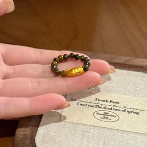 Detail of tiger eye bead ring featuring a golden lucky cat charm on a finger