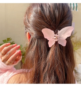 Detail of pink matte butterfly hair claw clip worn on hair with natural outdoor lighting
