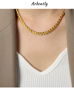 Detail shot of a golden wheat-chain necklace on a model wearing a brown blazer