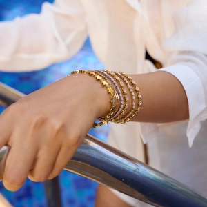 Detail of pink zircon gold bracelets layered on wrist by a pool, showing luxury heart charms
