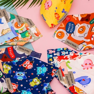 Flat lay of colorful cotton pet bandanas with handmade labels on blue and pink background
