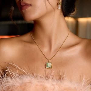Close-up of a vintage green enamel window butterfly necklace on a model wearing pink feathers