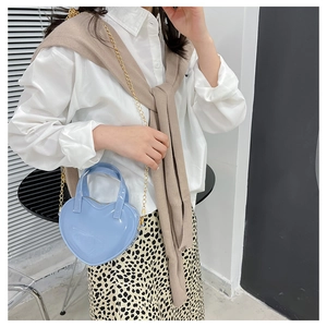 Detail of light blue heart-shaped patent leather crossbody bag with gold chain strap