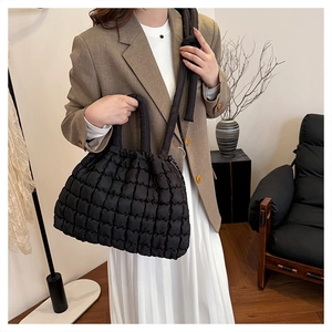 Detail of black pleated tote bag showing wrinkled texture and matching handle held by model