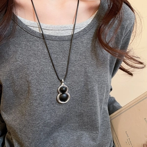 Détail d'un pendentif gourde vintage en bois sur un cordon noir porté par un mannequin