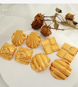 Collection of various geometric 18K gold plated titanium steel hoop earrings on white tray