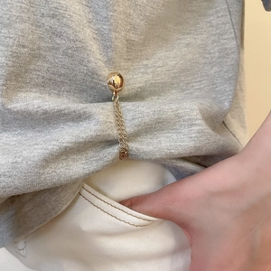 Detail of golden magnetic chain buckle for shortening T-shirt hems on gray cotton top