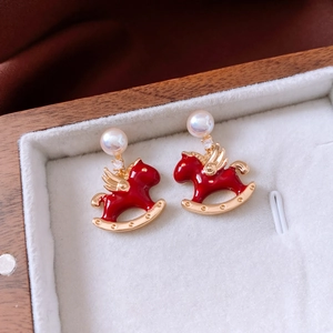 Macro detail of gold plated horse pendant earrings with red enamel and white pearl