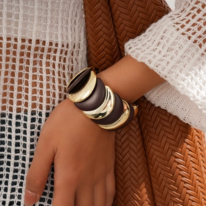 Dettaglio di un ampio bracciale in acrilico marrone e oro lucido sul polso