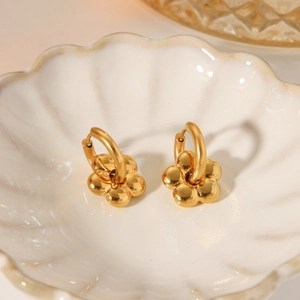 Detailed close-up of 18K gold plated flower earrings on a textured white ceramic plate