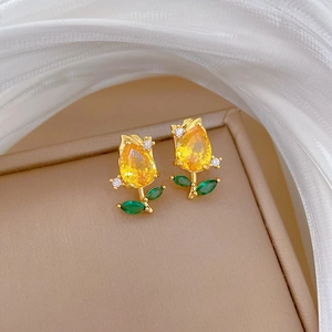 Detail of rose gold flower earrings with yellow teardrop stones and green leaf accents