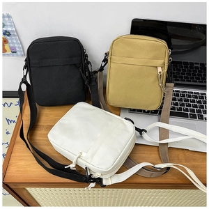 Three nylon crossbody bags in black, khaki, and white on a wooden desk with a laptop