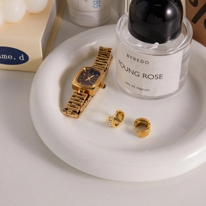Elegant gold square watch and zircon hoop earrings displayed on a white ceramic tray