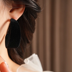 Close-up of a model wearing large black flocking C-shaped hoop earrings with velvet texture