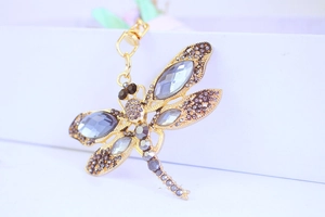 Detailed close-up of golden dragonfly keychain with dark grey crystals and rhinestones