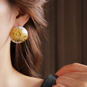 Close-up of vintage white round stud earrings with golden daisy relief on female model