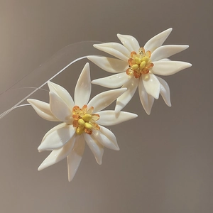 Detailed view of white resin flower earrings with yellow beaded centers and textured petals