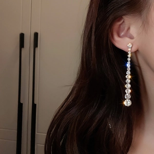 Macro detail of long silver tassel earrings with sparkling rhinestones worn on a model