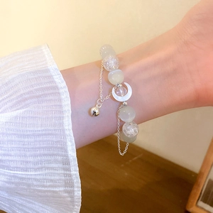 Close-up of cat eye stone bead bracelet with moon pendant and bell on woman's wrist
