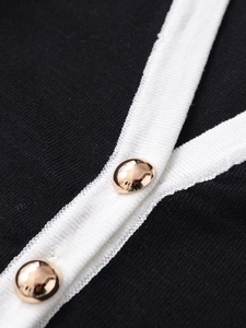 Detail of black knit dress featuring white contrast trim and gold round buttons