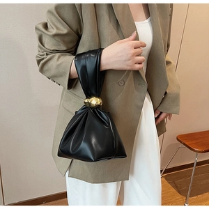 Detail of minimalist black pleated bucket bag featuring a large polished gold metal bead
