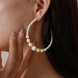 Detailed view of large C-shaped hoop earrings featuring elegant white faux pearls and gold beads