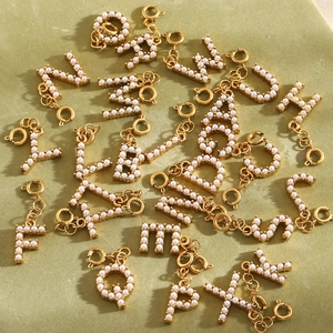 DIY gold 18K stainless steel alphabet pendants with white pearls on a green fabric backdrop