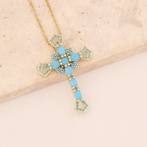 Detail of cross necklace with turquoise inlay on a textured beige stone base