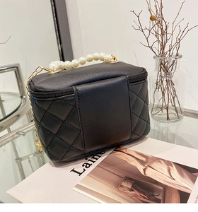 Detail of black quilted mini bucket bag with pearl handle and golden chain strap