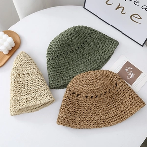 Flat lay of beige, dark green, and brown hand-woven straw sun hats on a white desk