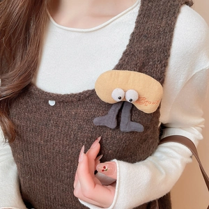 Detail of plush yellow character brooch with Beauty embroidery on brown sweater vest