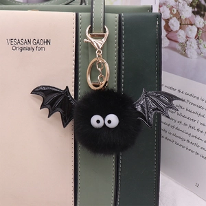 Black plush bat keychain with white eyes and wings hanging on a beige handbag