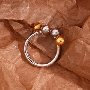 Detail of silver and gold beads on a minimalist open ring set against brown paper