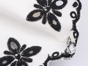 Close-up of black floral embroidery with hollow eyelets on soft white fabric