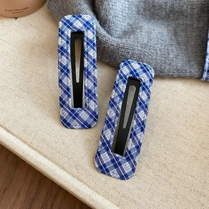 Close-up of blue and white checkered fabric rectangle hair clips on a soft linen background