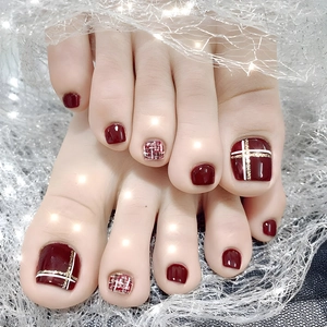 Close-up of wine red press-on toenails with gold plaid patterns and glitter backdrop