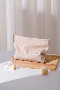 Dettaglio della trousse rosa chiaro con ricamo a farfalla bianca ed etichetta H&R BAG