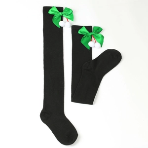 Detail of black over-knee Christmas socks with green bows and white fuzzy pom-poms