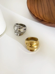 Detailed view of gold and silver wavy wide band rings on a minimalist display stand