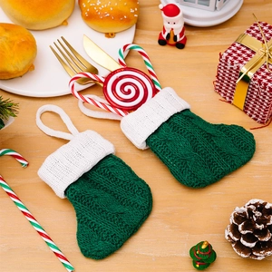 Mini green knit Christmas stocking cutlery holder with festive decorations on wood