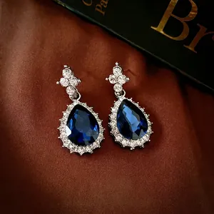 Luxurious silver earrings with teardrop blue sapphire and zircon on silk background