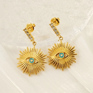 Gold evil eye earrings with blue stones and diamonds on white silk fabric background