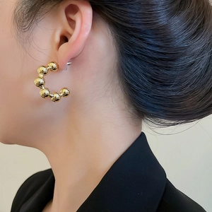 Close-up of golden beaded C-shaped hoop earring worn with a stylish black blazer