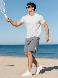 Men's white fitness t-shirt and grey shorts set shown in a bright outdoor beach setting