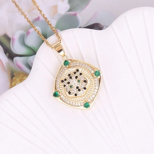 Macro detail of 18K gold leopard head pendant with emerald accents on a white shell