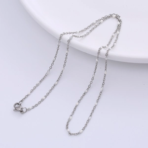 Detail of silver chain necklace with white beads and lobster clasp on white surface